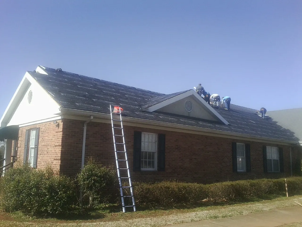 Crew tearing shingles off a brick ranch roof with a ladder set — Metal Roof Repair work by our crew in University Park