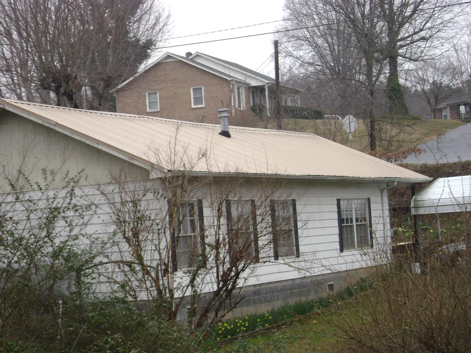 Tan metal roof on a white sided house set into a hillside — Commercial Roofing by Roofing Brothers in University Park